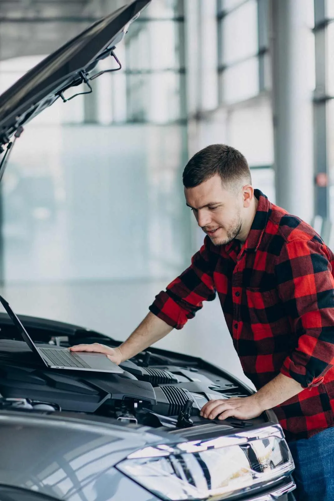 Man checking the open engine bay of a silver car with a laptop